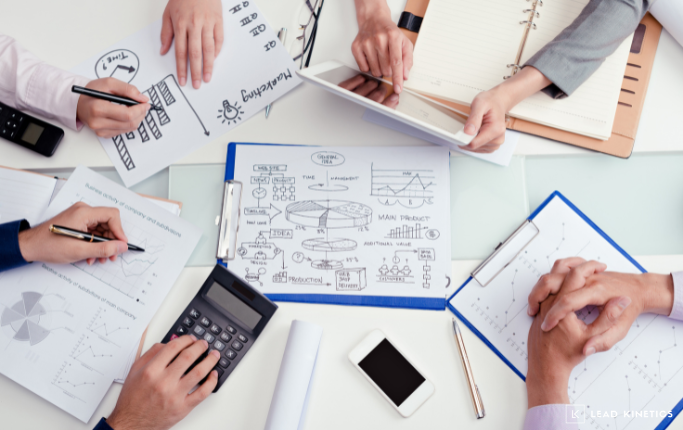 Team collaborating on a marketing brief with charts, graphs, and notes spread across a desk alongside a calculator, tablet, and smartphone – planning strategies for business growth.